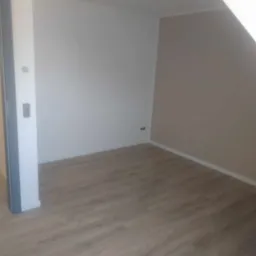 Pomalowane wnętrze poddasza z nową podłogą, ściany w odcieniach bieli i beżu, widoczne gniazdka elektryczne i listwa przypodłogowa.