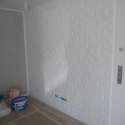 REMOLUKI ŁUKASZ LITWIŃSKI - Ściana w pokoju pokryta białą farbą imitującą cegłę, widoczne puszki z farbą i zaklejona podłoga.