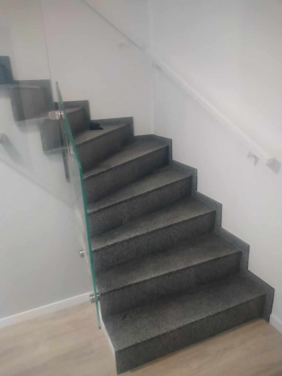 Granitowe schody z szklaną balustradą w jasnym wnętrzu domu w Bytowie, widok z dołu.