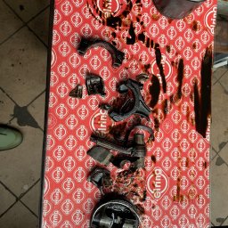 LAKIERNICTWO POJAZDOWE ZENON KARCZEWSKI w spadku - Rozłożony silnik samochodowy z wyciekającym olejem na kartonie Elring, widoczne elementy tłoka, korbowody i filtr oleju.