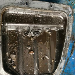LAKIERNICTWO POJAZDOWE ZENON KARCZEWSKI w spadku - Ociekacz oleju silnikowego z resztkami oleju i zanieczyszczeń, widoczne ślady użytkowania i korozji na metalowej obudowie.
