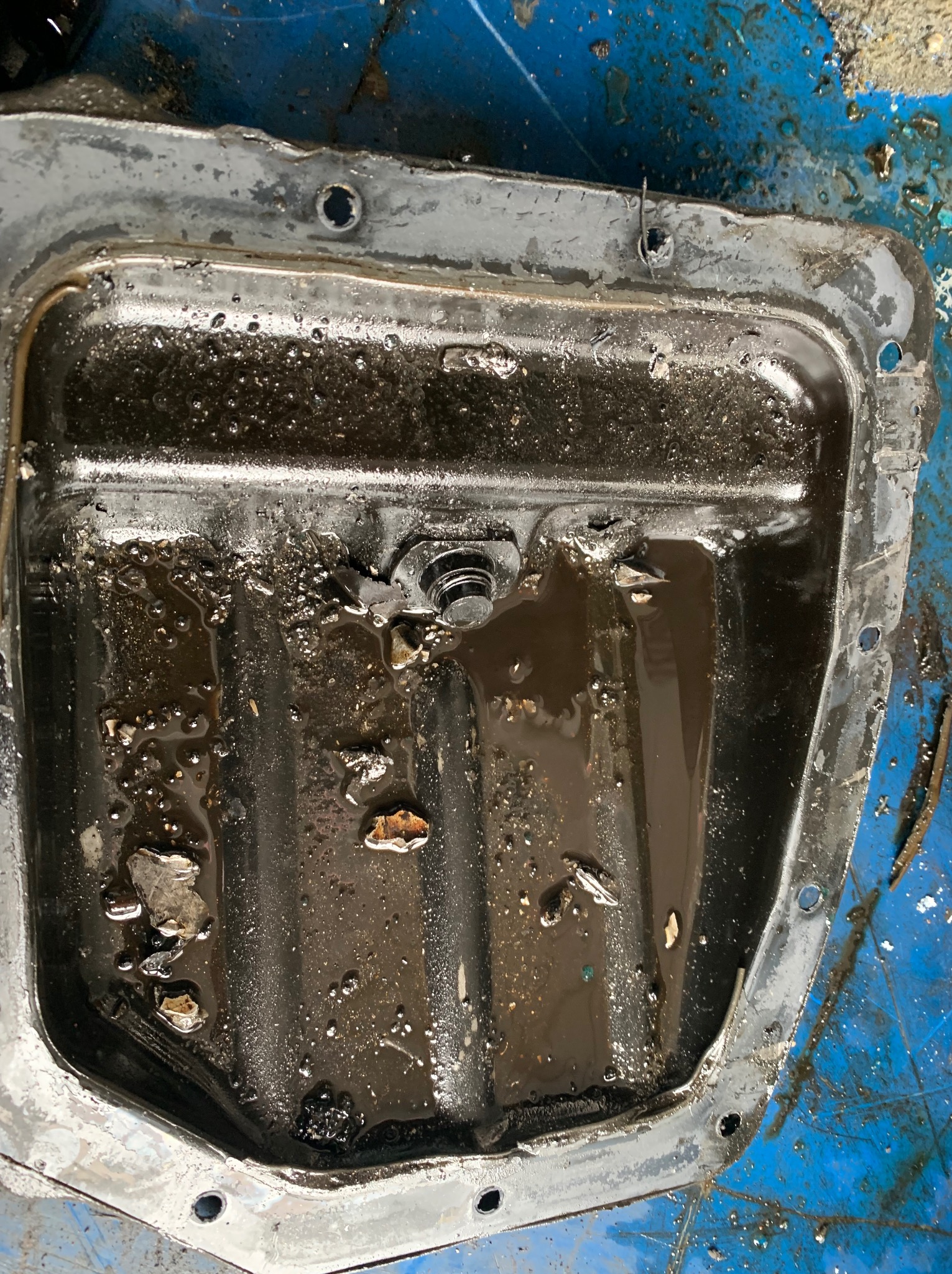 Ociekacz oleju silnikowego z resztkami oleju i zanieczyszczeń, widoczne ślady użytkowania i korozji na metalowej obudowie.