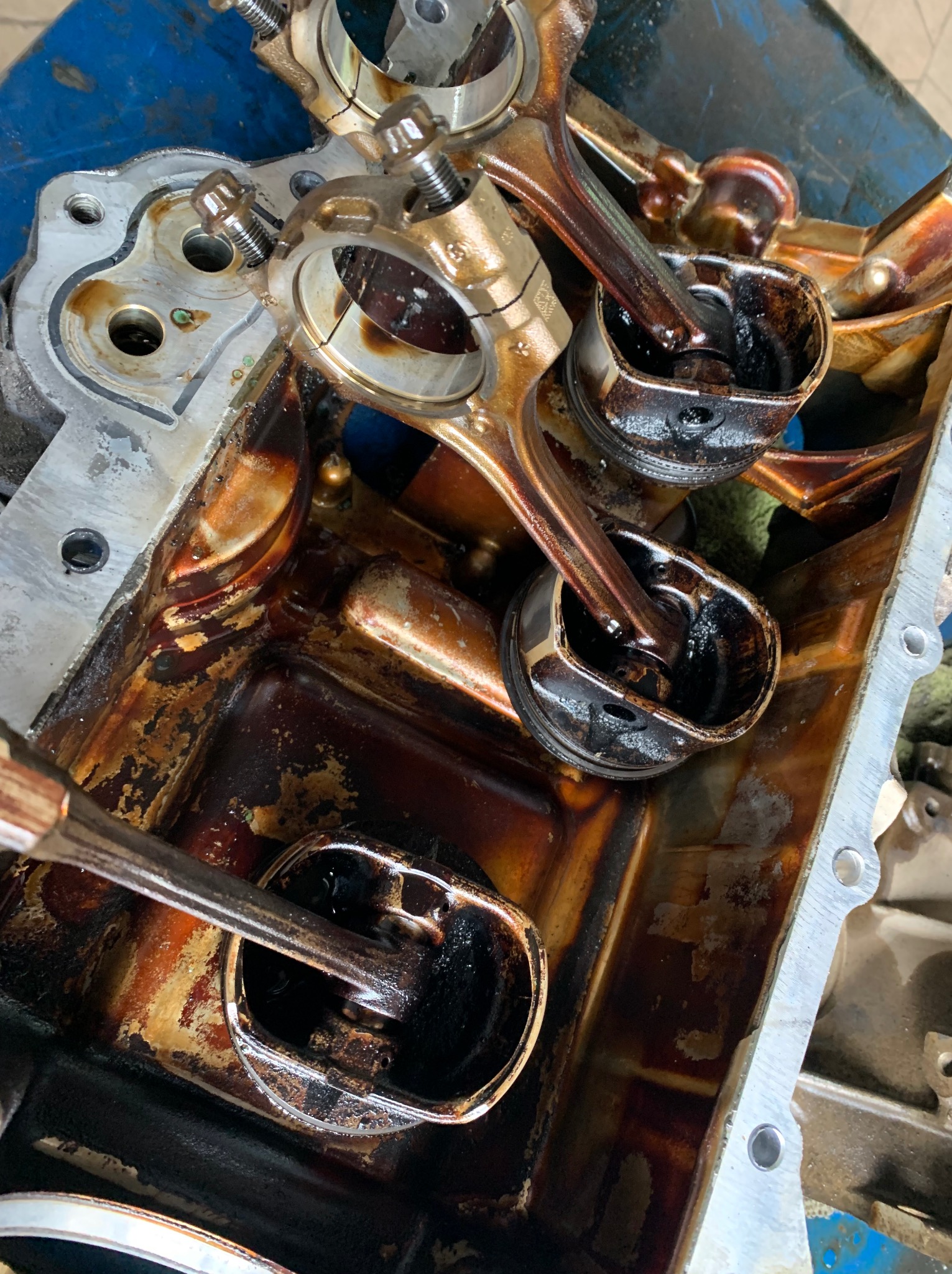 Olejem pokryte tłoki i korbowody silnika samochodowego, widoczne ślady zużycia na elementach.