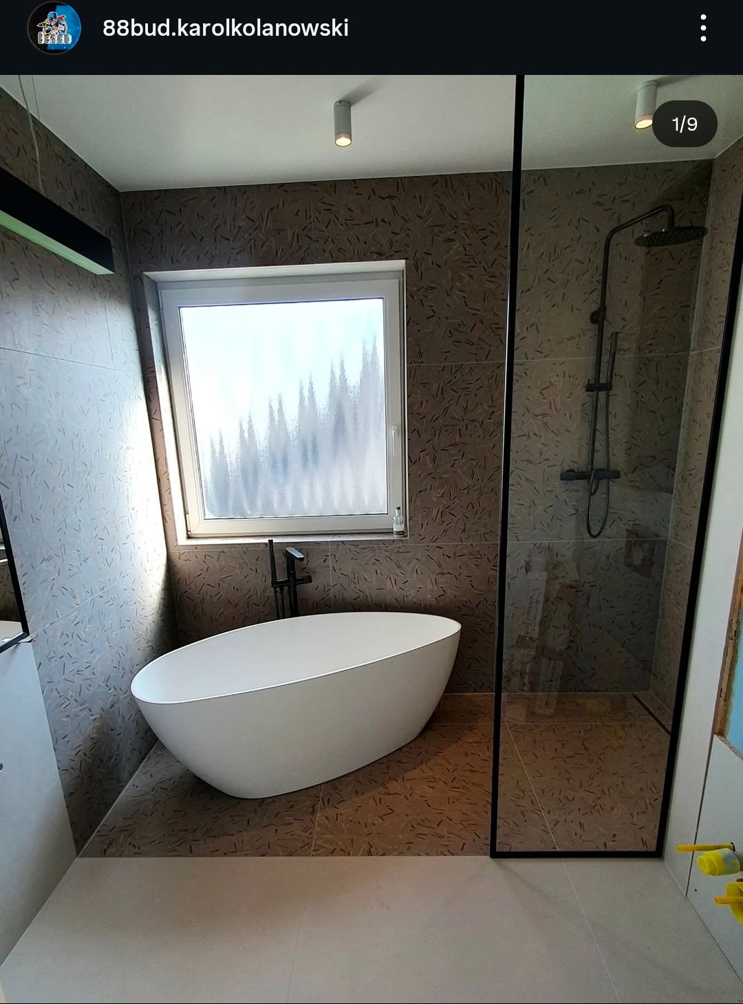 Nowoczesna łazienka z wolnostojącą wanną, kabiną prysznicową typu walk-in i oknem z widokiem na zalesione wzgórza. Brązowe płytki z unikalnym wzorem na ścianach i podłodze.