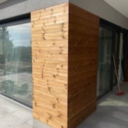 WIDAM Adam Wicha Usługi Remontowo-Budowlane - Drewniana obudowa narożna na zewnątrz budynku, z widocznym fragmentem okna i przesuwnych drzwi balkonowych, oraz częścią tarasu. Widoczne poziome deski z naturalnym usłojeniem drewna.