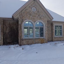 Adam - Kamienny dom z dwoma łukowymi oknami i jednym prostokątnym, pokryty śniegiem, z widocznymi śladami na śniegu.