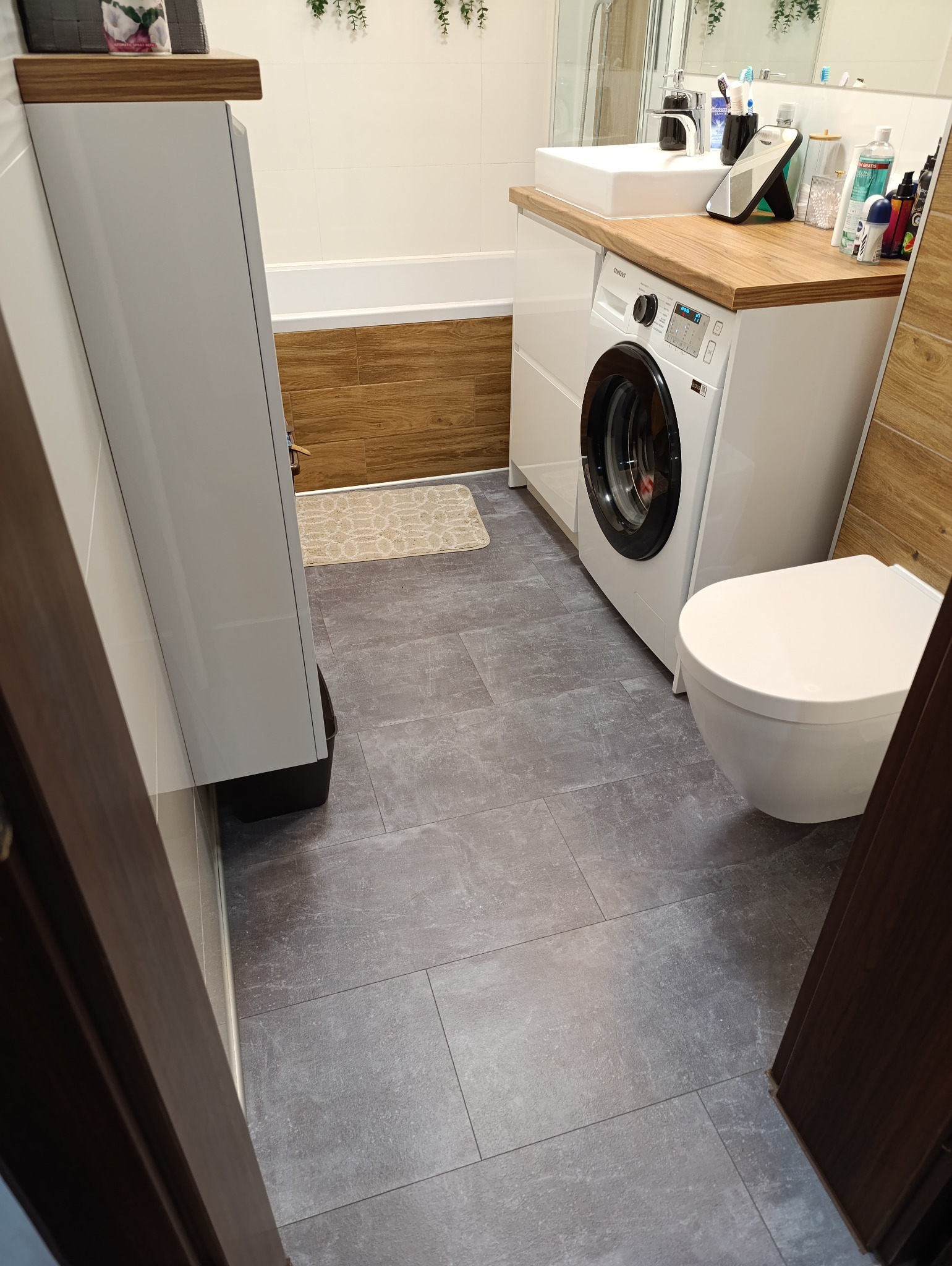 Szare, prostokątne panele podłogowe imitujące kamień w łazience w Jangrocie, ułożone z przesunięciem, widoczne fragmenty zabudowy wanny, pralki i toalety.