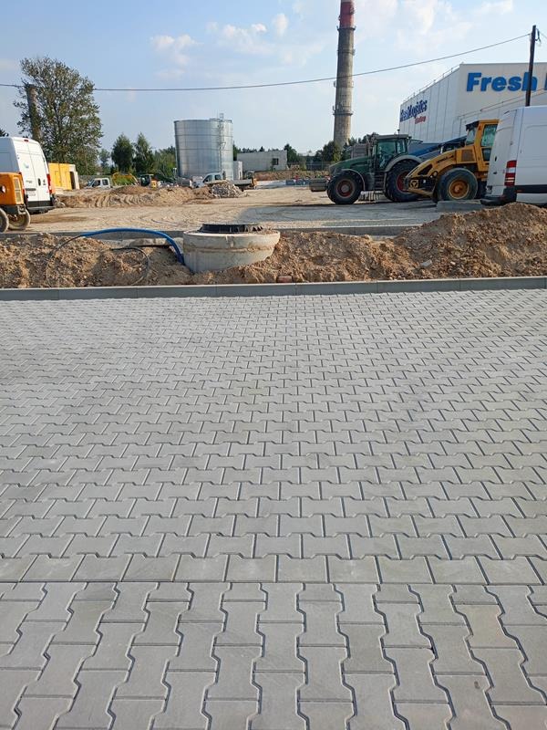 Nowo ułożona szara kostka brukowa typu I na placu budowy z widocznymi maszynami budowlanymi i wykopem w tle.