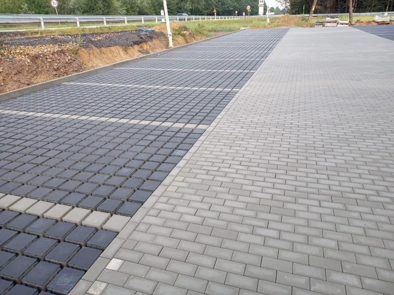 Nawierzchnia parkingu z częściowo ułożoną szarą kostką ażurową i jasnoszarą kostką brukową, widok z góry.