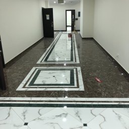 Yurii Antymeniuk - Korytarz z nową podłogą wyłożoną brązowymi i białymi płytkami imitującymi marmur, z dekoracyjnymi wstawkami i listwami, widok na drzwi z numerem 20 i dalszą część korytarza.