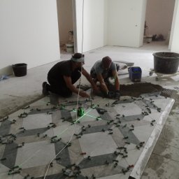 Yurii Antymeniuk - Dwóch mężczyzn układa wzorzystą podłogę z płytek, używając poziomicy laserowej i klipsów dystansowych w surowym wnętrzu.