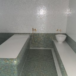 Yurii Antymeniuk - Wnętrze łaźni wykończone mozaiką w odcieniach bieli, zieleni i złota, z umywalką w kształcie misy i złotą armaturą.