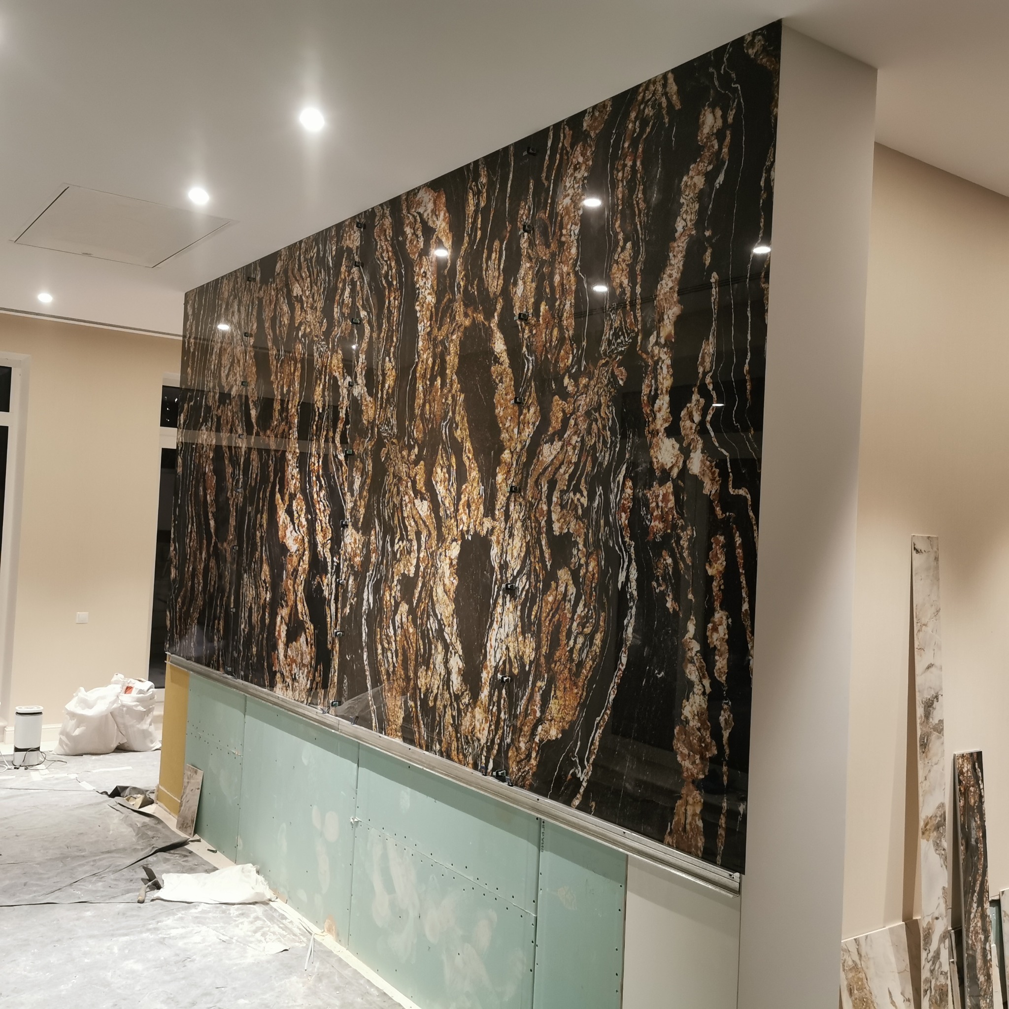 Ściana wykończona czarnym, polerowanym kamieniem z brązowymi i złotymi żyłami, zamontowana na płycie kartonowo-gipsowej w trakcie prac wykończeniowych.