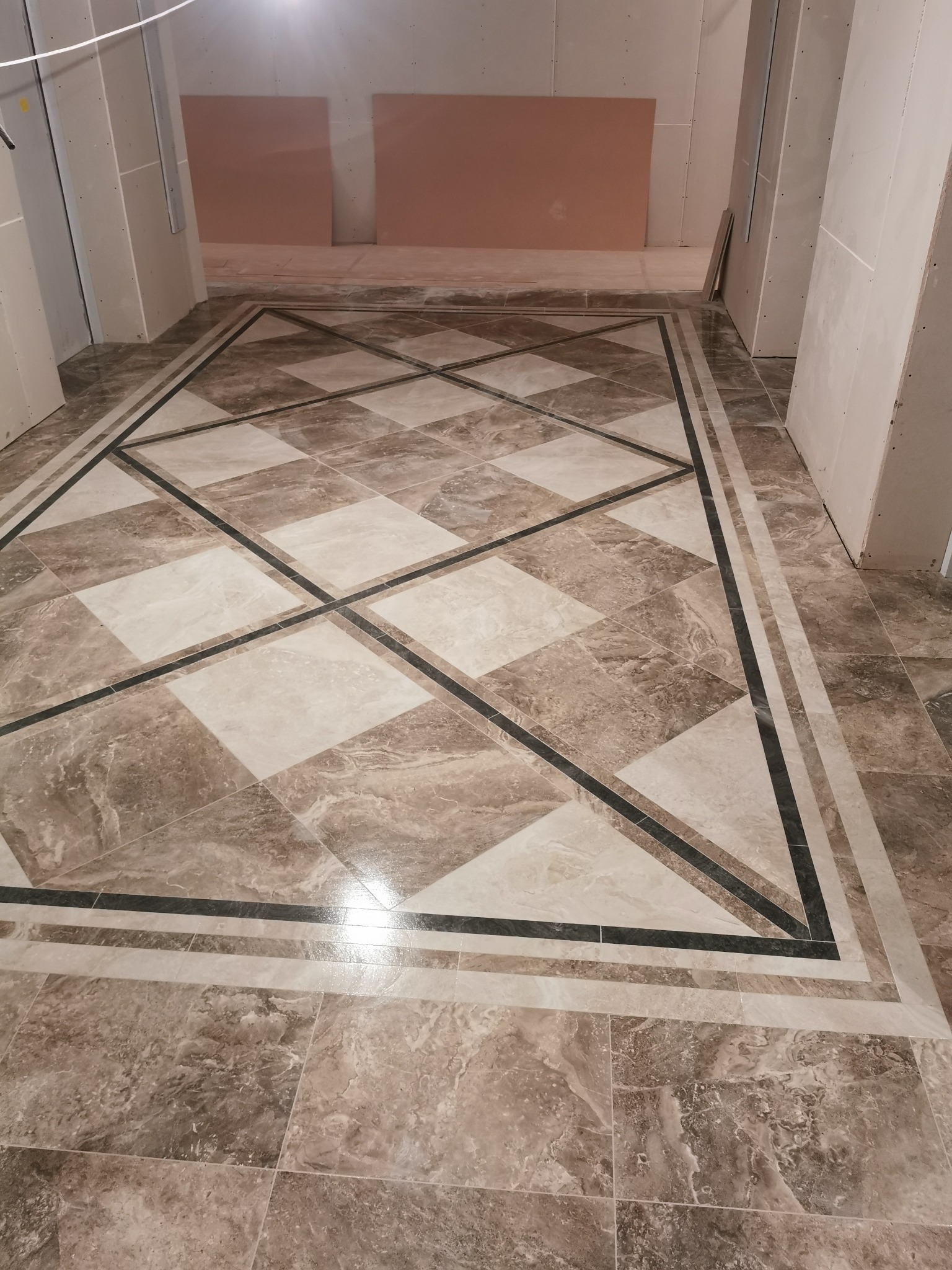 Wzorzysta podłoga z płytek w odcieniach beżu i bieli, z czarnymi akcentami, w surowym wnętrzu w trakcie wykończenia.