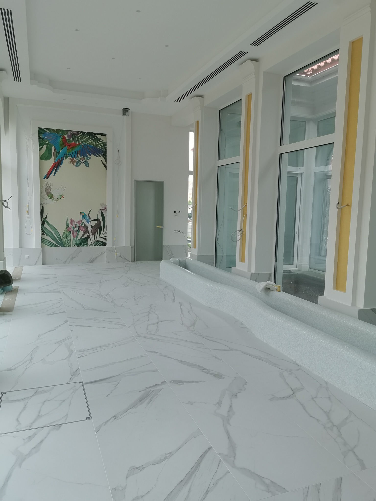 Jasne wnętrze z marmurową posadzką, dekoracyjnym malowidłem z motywem papug na ścianie i mozaikową fontanną wzdłuż okien.