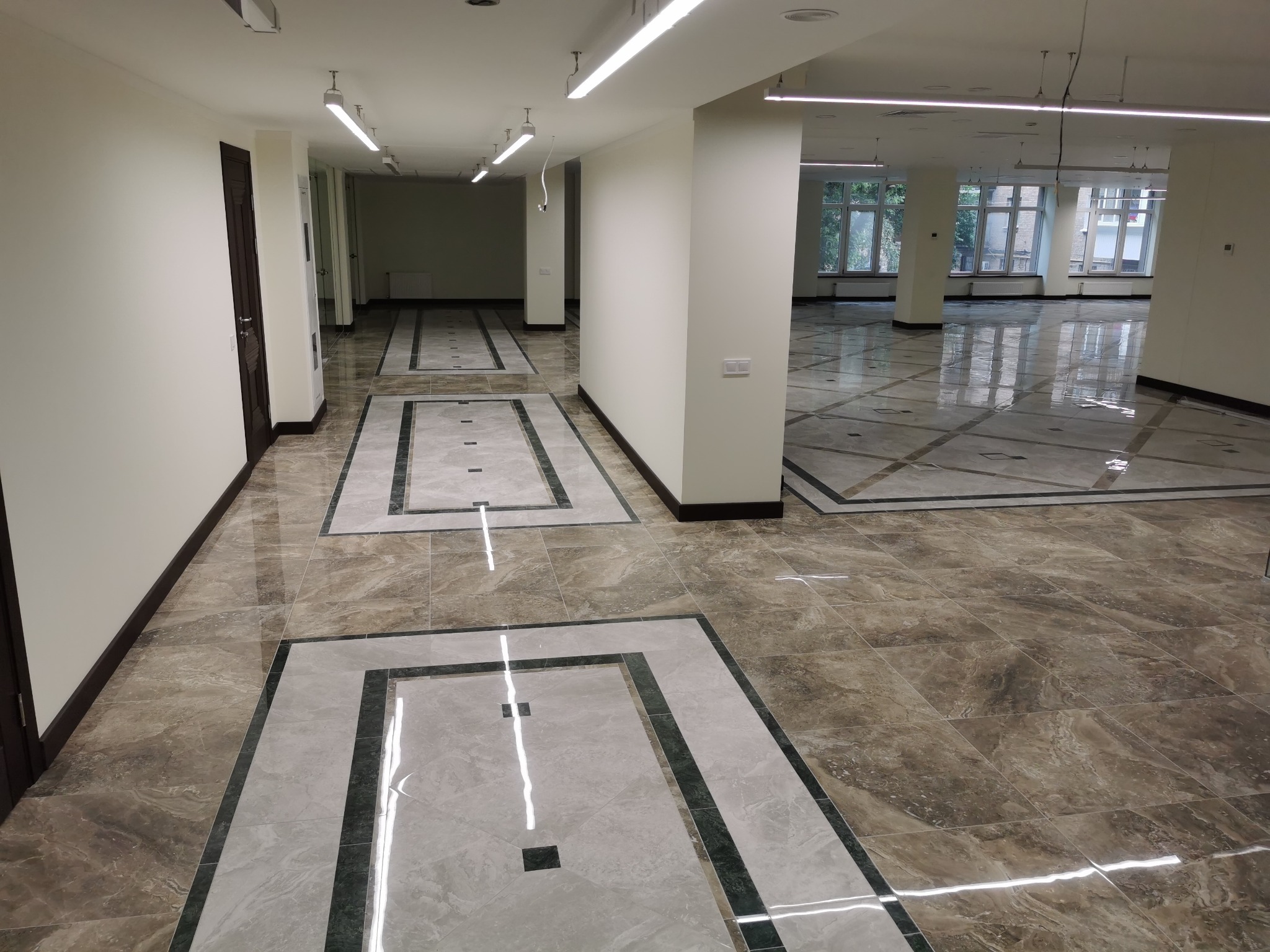 Wykończona posadzka z płytek w korytarzu biurowym, z wzorem geometrycznym, jasne ściany, oświetlenie liniowe.