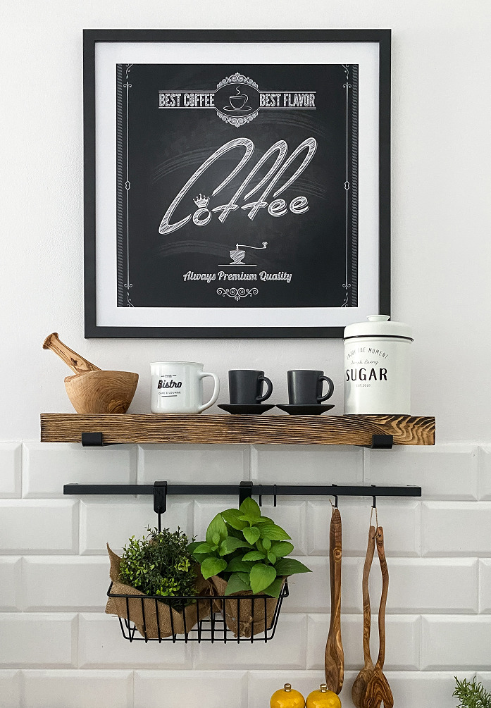 Dekoracyjna półka w kuchni z drewnianymi akcentami, ziołami w doniczkach i plakatem z motywem kawy na białej ścianie z kafelkami.