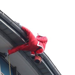 Hedgehog rope access jobs - Osoba przebrana za Świętego Mikołaja, na linie, zwisa z rynny budynku podczas potencjalnego czyszczenia. Widoczny kubeł zawieszony na linie.