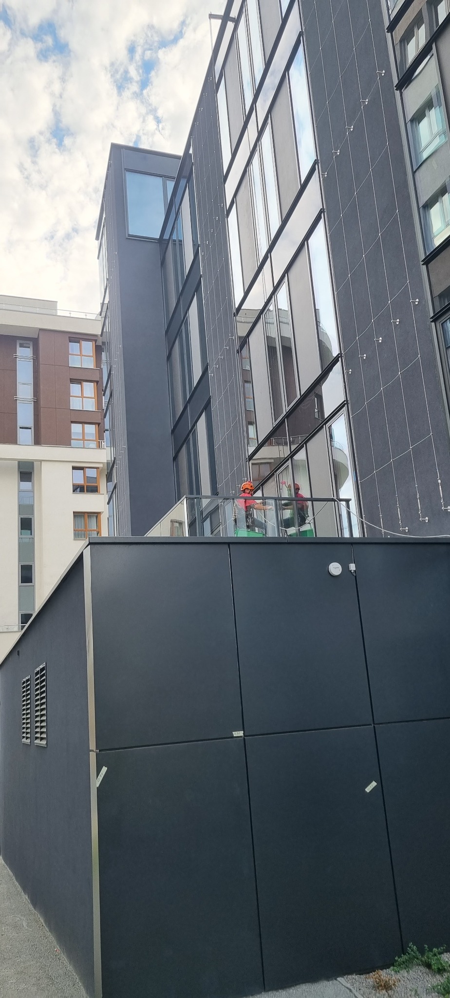 Pracownicy w kaskach na wysokościach czyszczą szklaną fasadę nowoczesnego budynku biurowego, widok z dołu.