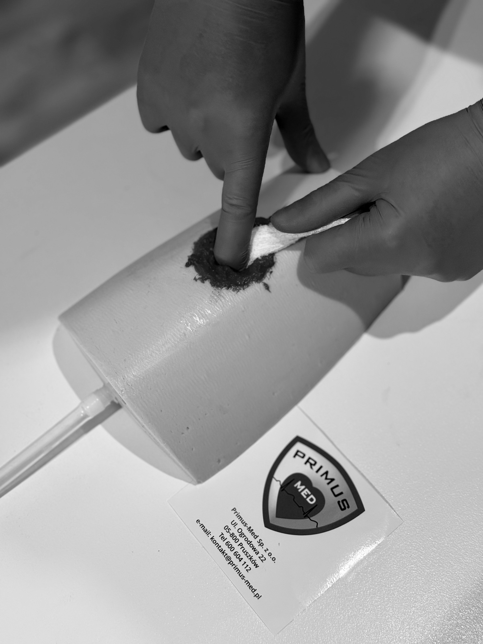 Opatrywanie rany na fantomie treningowym przez osobę w rękawiczkach, widoczne logo Primus MED