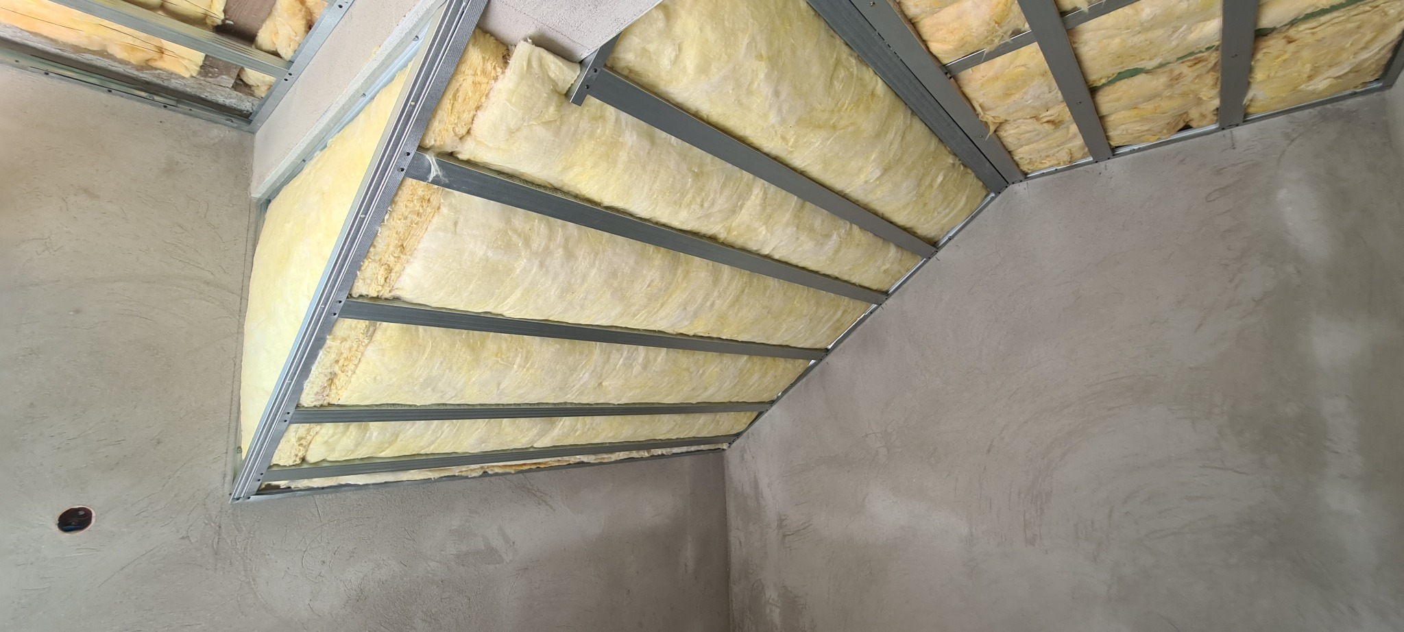 Niedokończona izolacja poddasza z wełny mineralnej w metalowej konstrukcji, surowe ściany przygotowane do dalszych prac wykończeniowych.