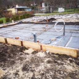 PWMS-BUD SPÓŁKA Z OGRANICZONĄ ODPOWIEDZIALNOŚCIĄ - Przygotowanie podłoża pod fundamenty: drewniany szalunek, zbrojenie stalowe, folia hydroizolacyjna i instalacja kanalizacyjna w gruncie z widocznymi śladami śniegu.