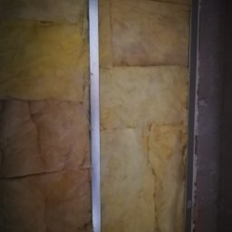 PWMS-BUD SPÓŁKA Z OGRANICZONĄ ODPOWIEDZIALNOŚCIĄ - Izolacja z wełny mineralnej zamontowana na ścianie, widoczne metalowe profile konstrukcyjne.