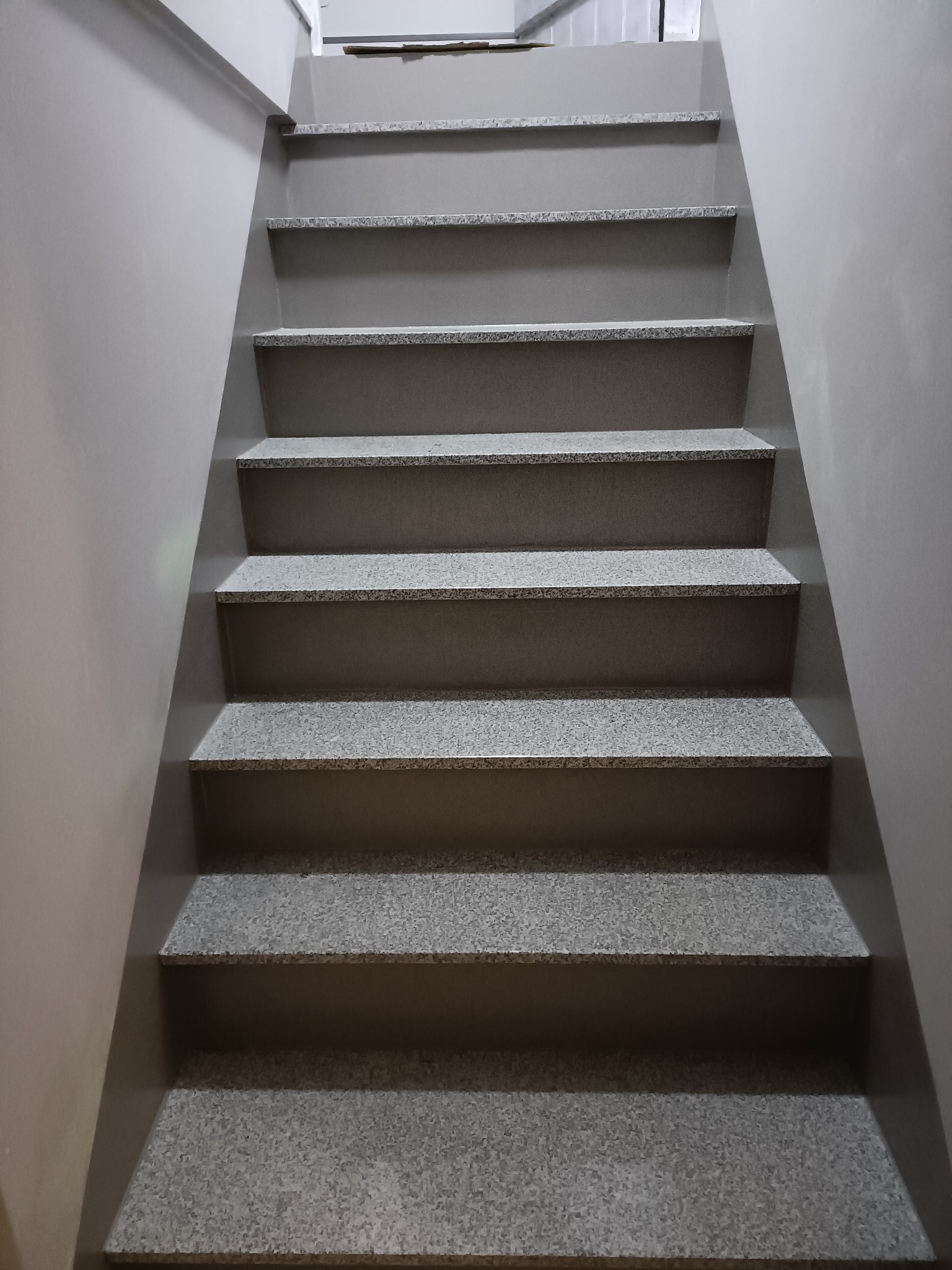 Schody wewnętrzne wykończone szarym gresem z widoczną fakturą, ściany pomalowane na jednolity szary kolor, minimalistyczne wykończenie.