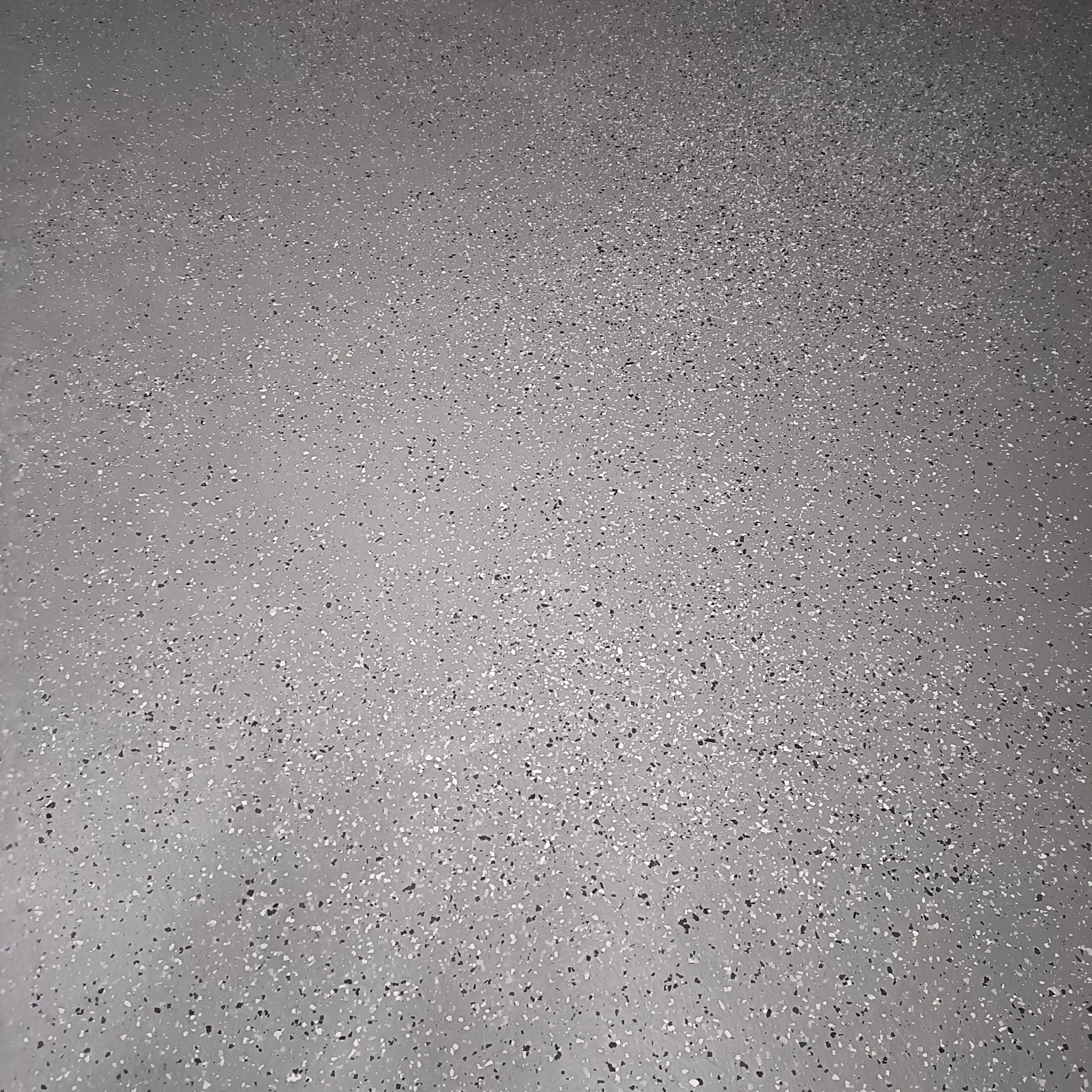Szara, jednolita posadzka żywiczna z drobnymi, czarnymi i białymi płatkami, tworzącymi wzór terrazzo.