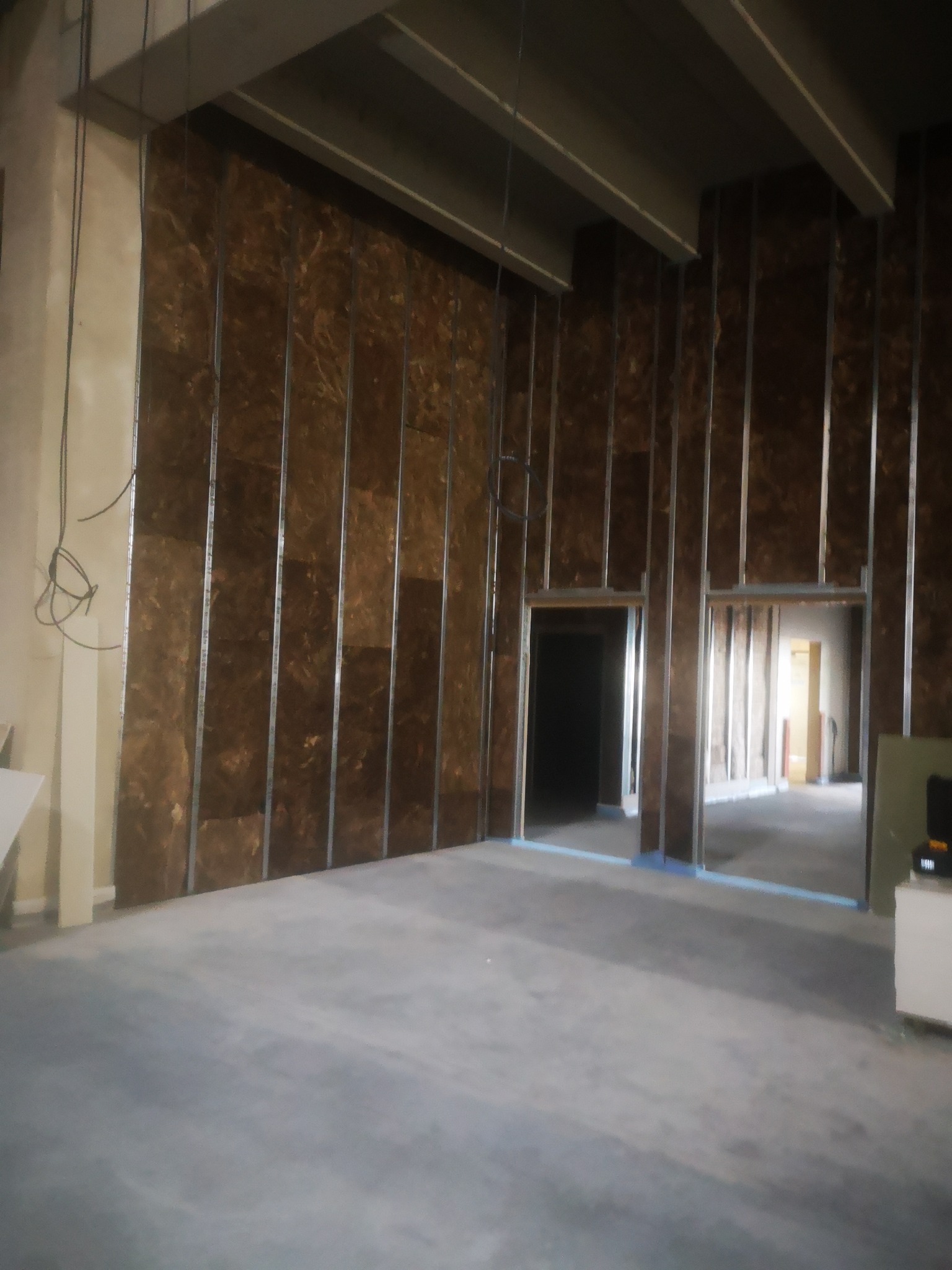 Wnętrze w trakcie prac: ściany z płyt OSB na metalowym stelażu, przygotowane otwory drzwiowe z niebieską taśmą zabezpieczającą, surowy beton na podłodze, widoczne kable na ścianie po lewej.