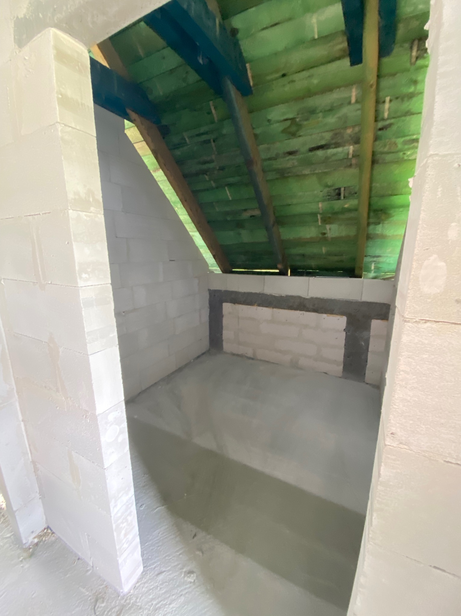 Wnętrze w trakcie budowy: ściany z białych bloczków, świeżo wylana podłoga z betonu, drewniany strop. Widok na surowy stan pomieszczenia.