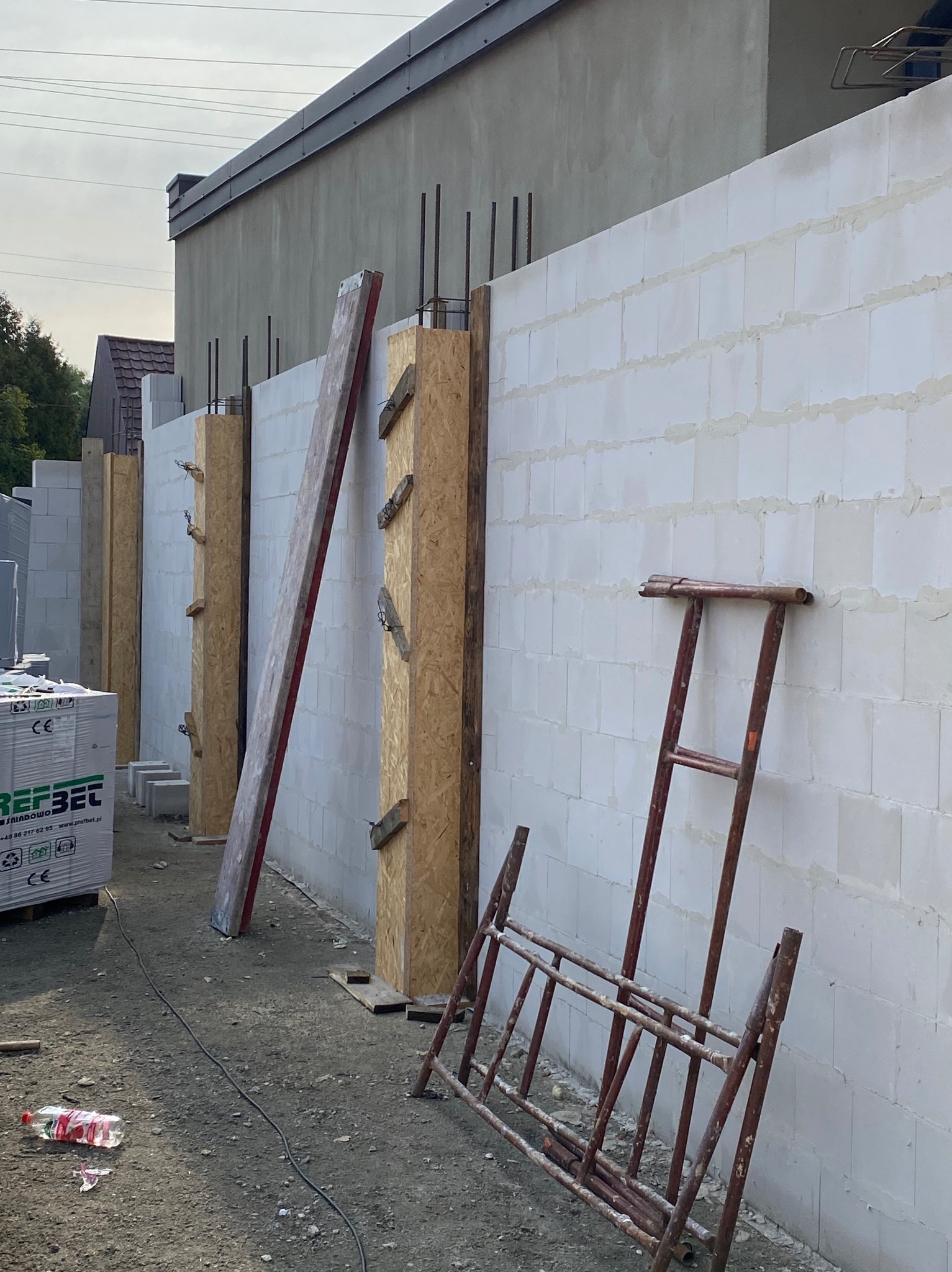 Budowa ściany z betonu komórkowego w Lucynowie Dużym. Widoczne szalunki, zbrojenie i paleta bloczków. Konstrukcja w trakcie realizacji, drabina oparta o ścianę.