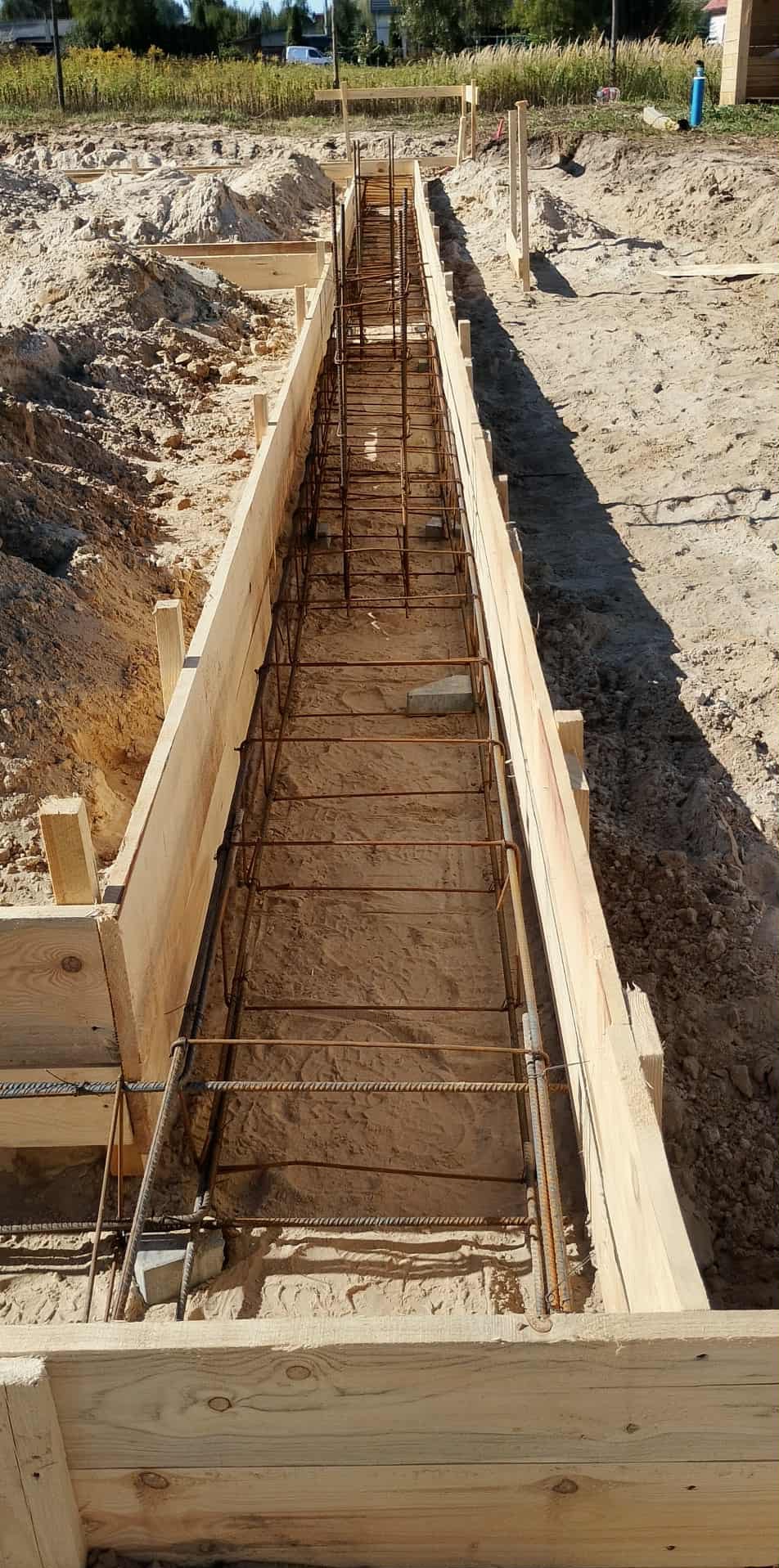 Szczegółowe ujęcie z góry na wykop z drewnianym szalunkiem i zbrojeniem ze stali, przygotowany pod wylanie fundamentów budynku.