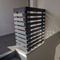 KUNTSTSCHMIEDE BEDNARSKI PIOTR - Nowoczesna, pozioma balustrada schodowa z metalowych profili w odcieniach szarości, zamontowana na schodach wewnątrz budynku, z widocznym fragmentem kartonu wewnątrz konstrukcji.