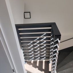 KUNTSTSCHMIEDE BEDNARSKI PIOTR - Nowoczesna, metalowa balustrada schodowa z poziomymi panelami, rzucająca geometryczne cienie na szare schody i podłogę, widok z góry.