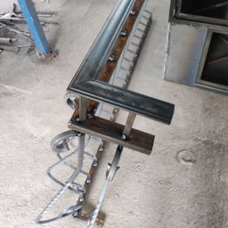 KUNTSTSCHMIEDE BEDNARSKI PIOTR - Element metalowej konstrukcji z dekoracyjnymi spiralnymi zdobieniami, spawany z profili, w warsztacie.