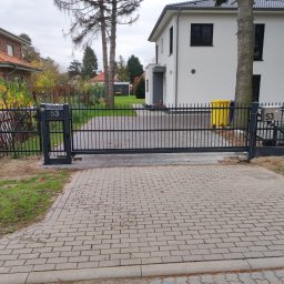 KUNTSTSCHMIEDE BEDNARSKI PIOTR - Czarna, przesuwna brama wjazdowa z numerem domu 53, widoczna z zewnątrz posesji, z brukowanym podjazdem i pracownikiem w tle.