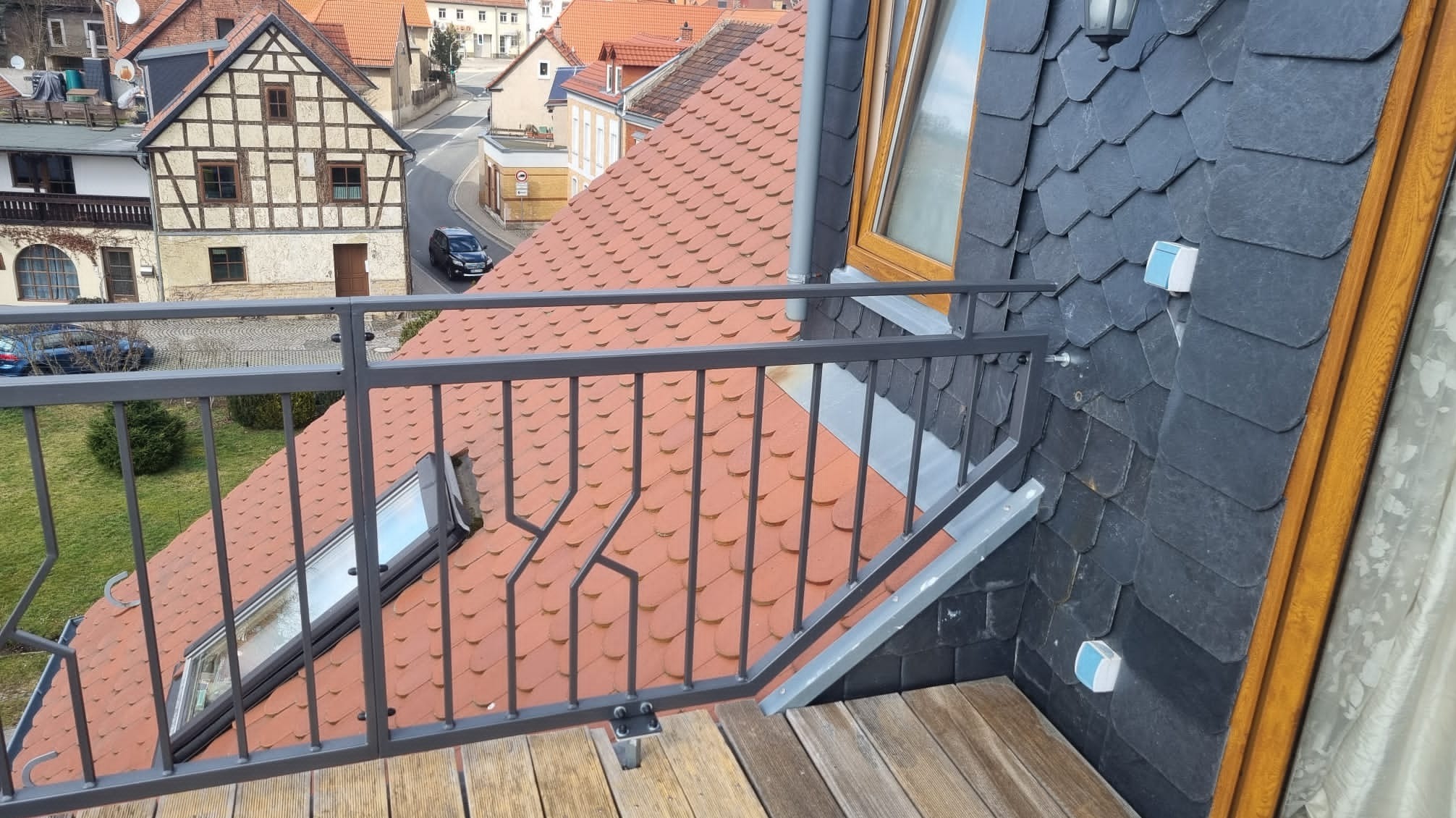 Szary metalowy balkon z widokiem na miasto z czerwonymi dachami i budynkiem z muru pruskiego