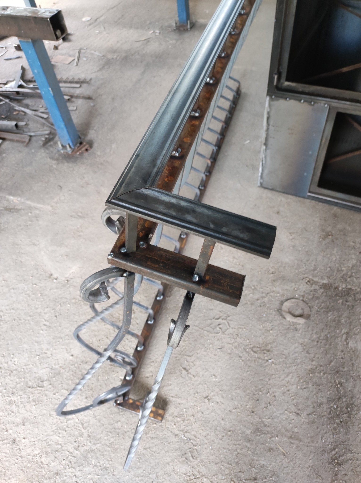 Element metalowej konstrukcji z dekoracyjnymi spiralnymi zdobieniami, spawany z profili, w warsztacie.