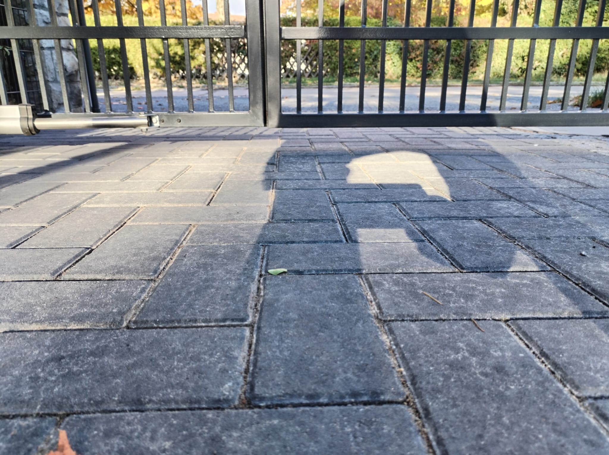 Automatyczna brama wjazdowa z czarnego metalu widziana z poziomu kostki brukowej w Gubinie, z widocznym siłownikiem i cieniem na nawierzchni.