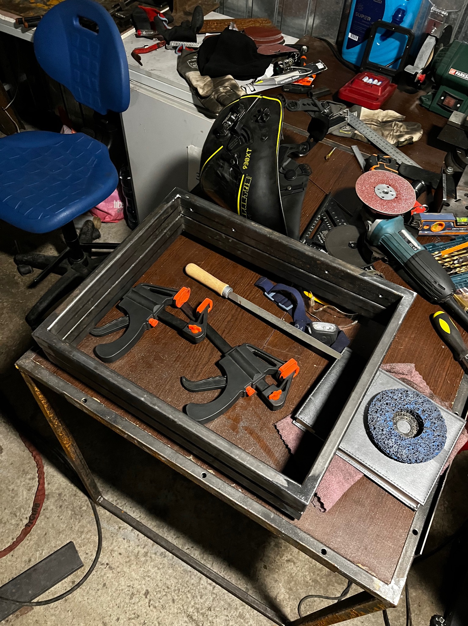 Metalowa rama spawana z profili, zabezpieczona zaciskami stolarskimi, widoczna na warsztatowym stole z narzędziami i akcesoriami do obróbki metalu.