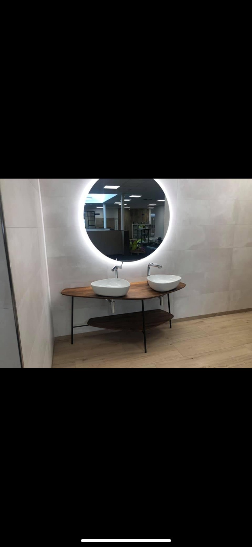 Nowoczesna łazienka z dwoma umywalkami wpuszczonymi w drewniany blat na metalowym stelażu i okrągłym lustrem z podświetleniem LED.