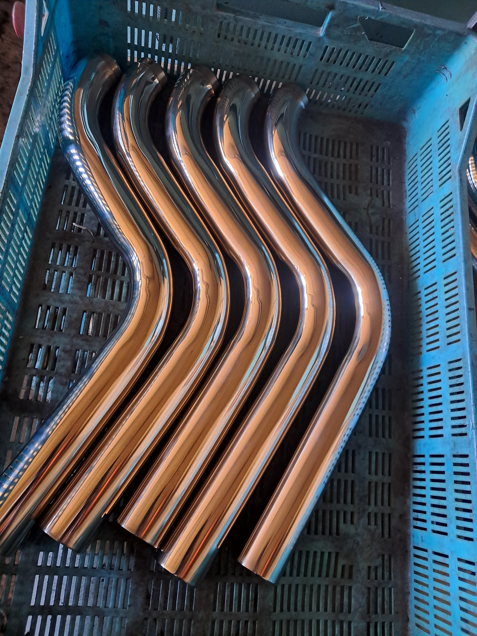 Rząd wygiętych, lśniących rur ze stali nierdzewnej w niebieskim plastikowym pojemniku z otworami.