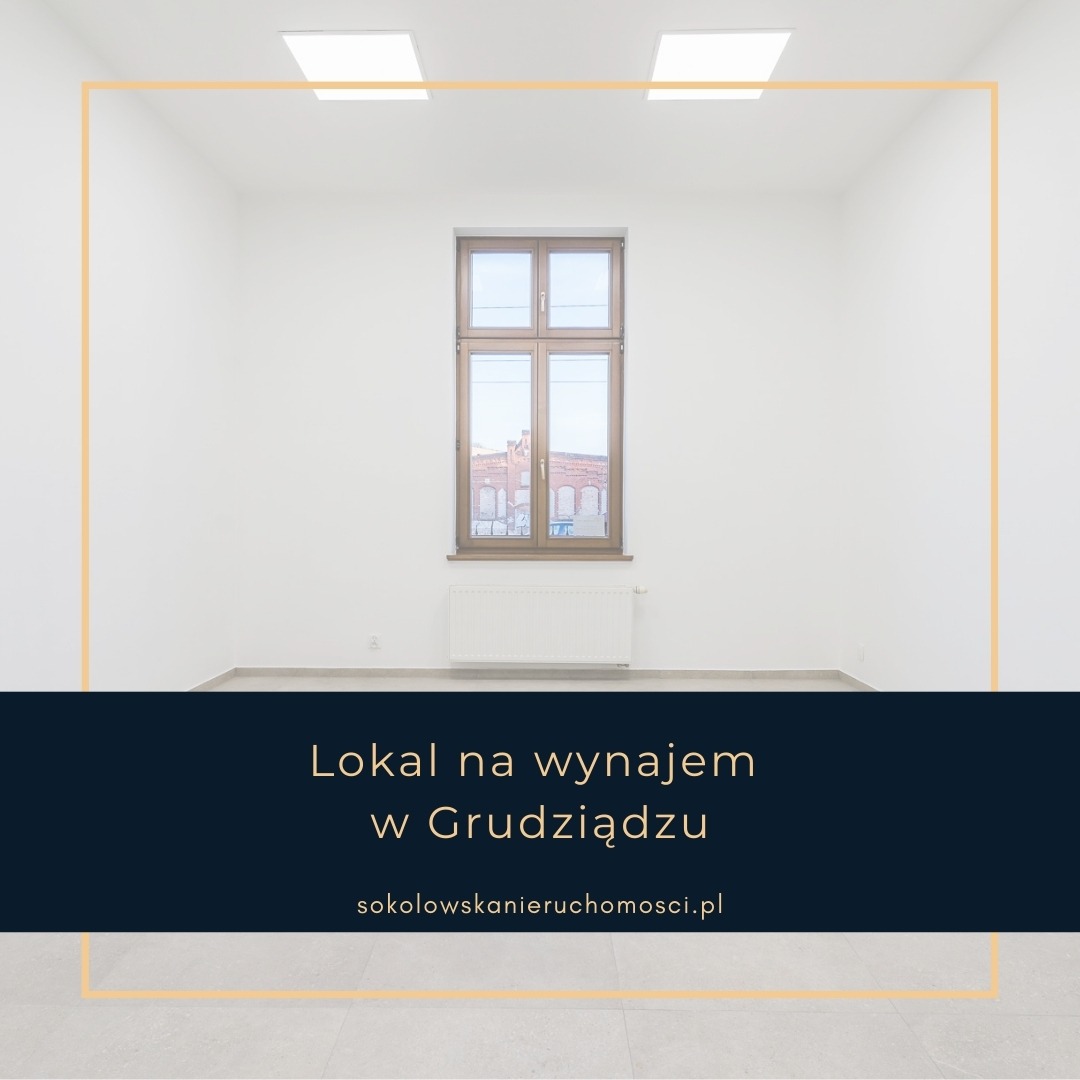 Puste, jasne pomieszczenie z oknem, widok na ceglany budynek przez okno, białe ściany, szara podłoga, grzejnik pod oknem, dwie lampy sufitowe.