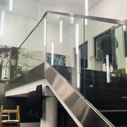 POLER-MET MAREK UDZIK - Wnętrze z zamontowaną szklaną balustradą na schodach, widoczny pracownik w trakcie montażu, drabina oparta o ścianę, kartony i narzędzia w tle.