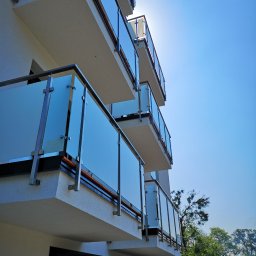POLER-MET MAREK UDZIK - Nowoczesny budynek z balkonami zabezpieczonymi balustradami szklanymi na metalowych wspornikach, widok z dołu w słoneczny dzień.