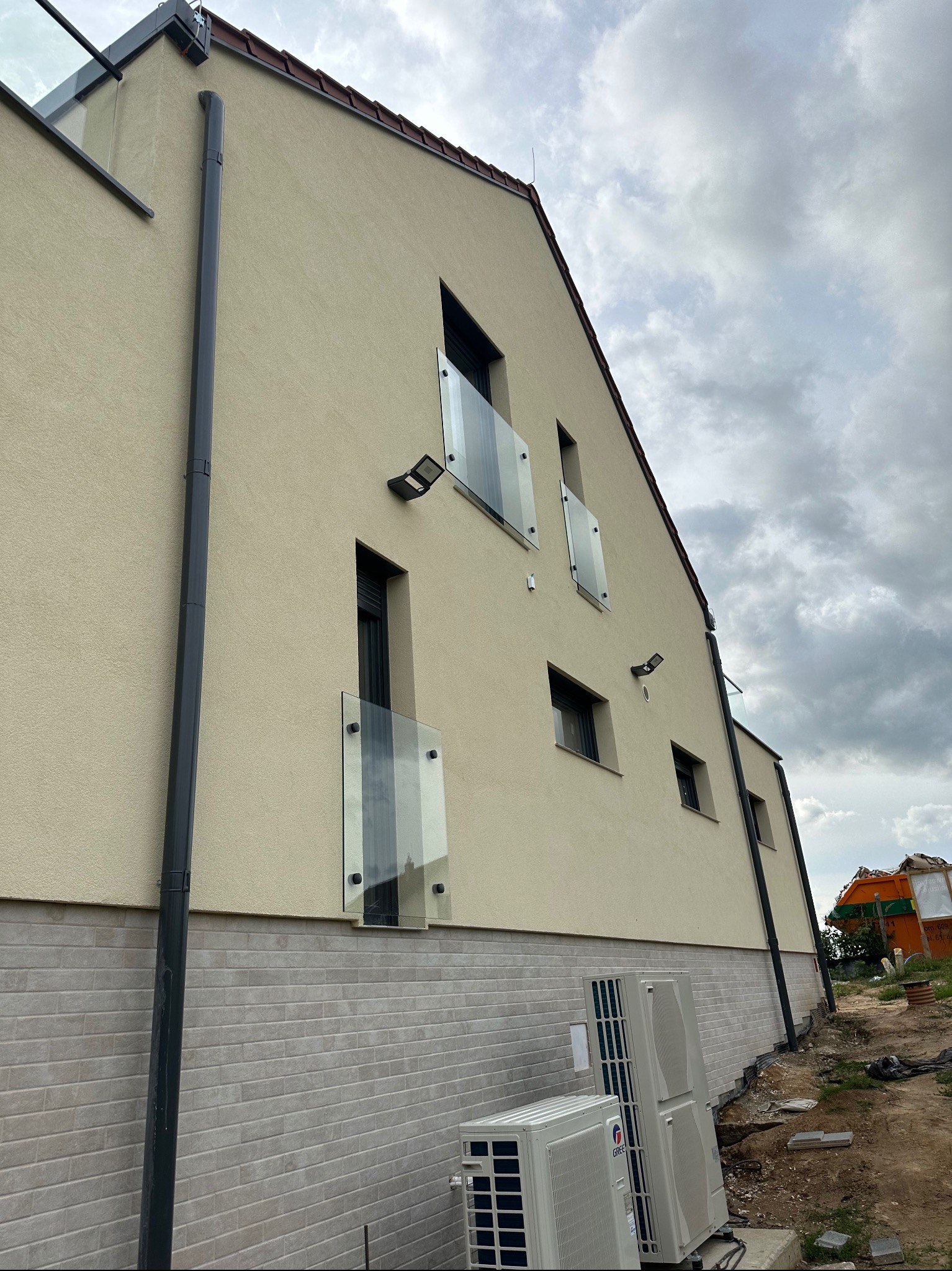 Nowoczesny dom z elewacją w odcieniach beżu i szarości, z minimalistycznymi balkonami z przezroczystymi taflami szkła, widoczne również klimatyzatory na zewnątrz budynku.