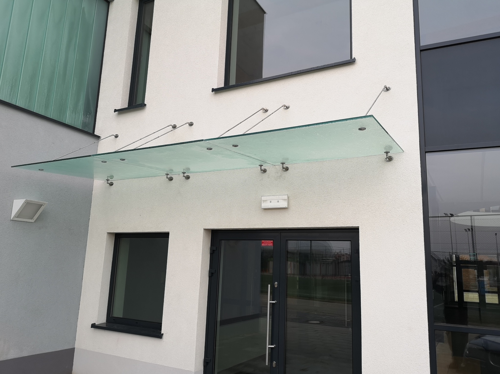 Szklany daszek nad wejściem do budynku w Czarnkowie, wsparty na metalowych wspornikach, widok z dołu.