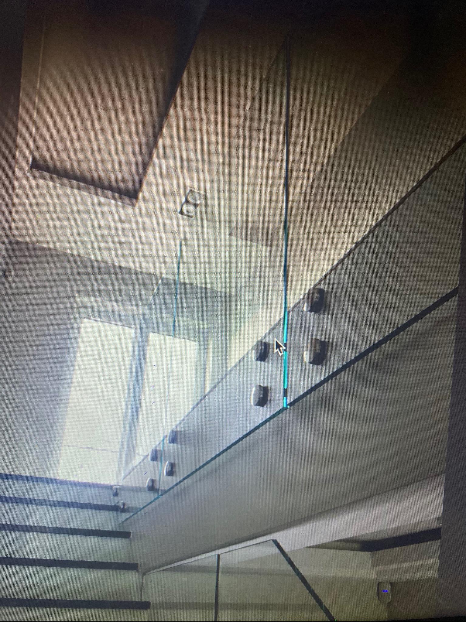 Szklana balustrada zamocowana na metalowych wspornikach, zabezpieczająca schody z widocznym oknem w tle.