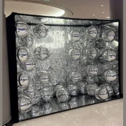 Błyszcząca fotobudka z srebrnymi kulami i neonowym napisem 'Enjoy the moment' w nowoczesnym wnętrzu.